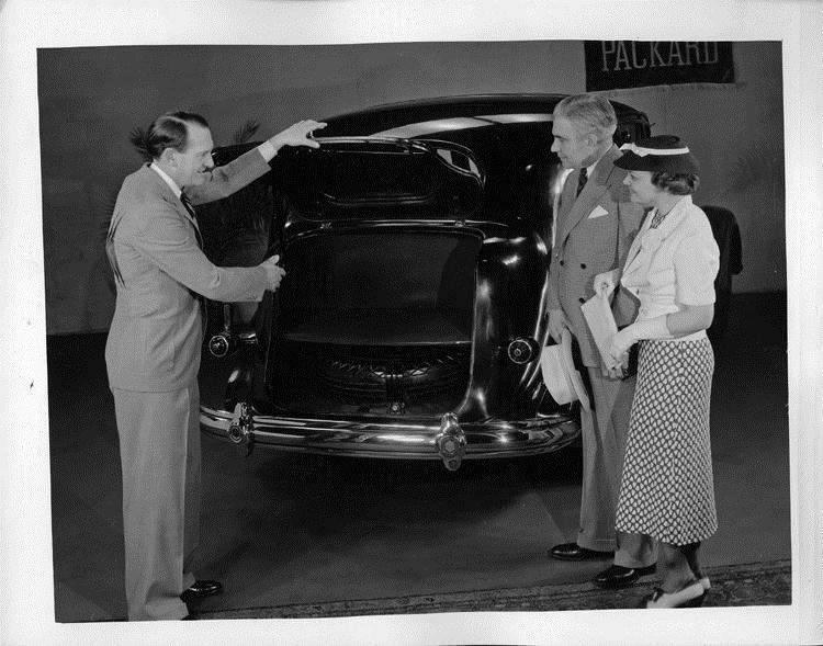 1937 Packard touring sedan, salesman showing trunk to couple