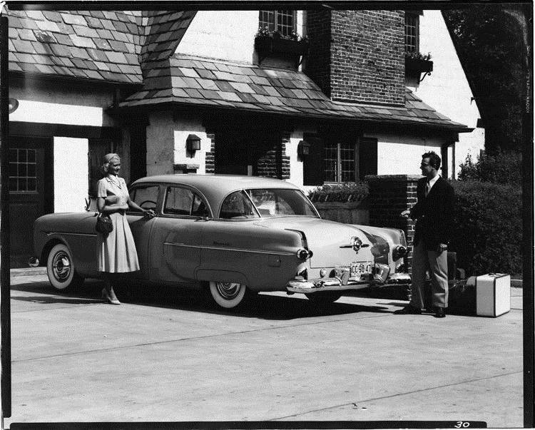 1951 Packard sedan, female standing at driver's door, man standing at rear of car