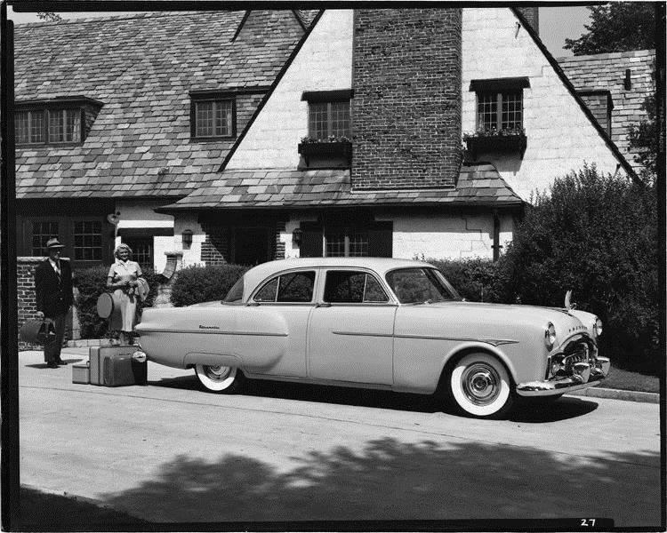 1951 Packard sedan, parked in driveway, couple standing near rear of car with luggage