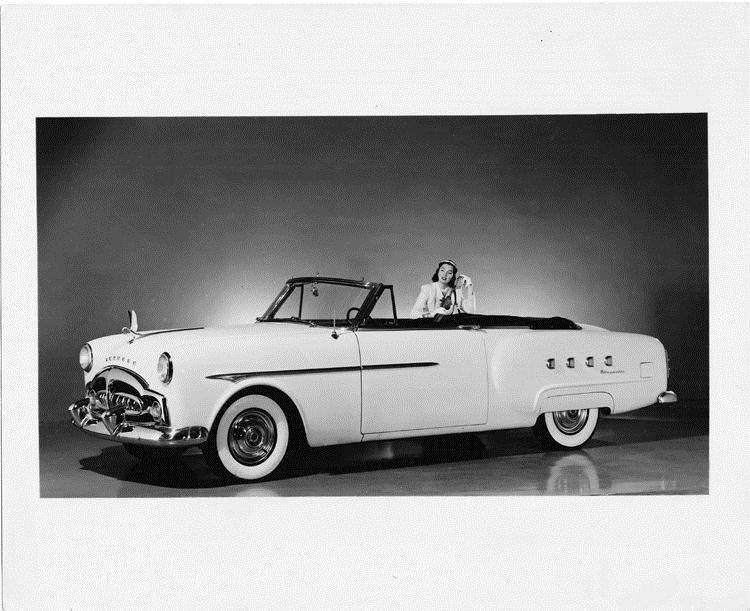 1951 Packard convertible, top folded, female leaning right passenger side of car