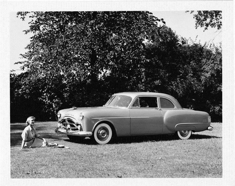 1951 Packard 200 club sedan, parked on grass, female sitting near front of car