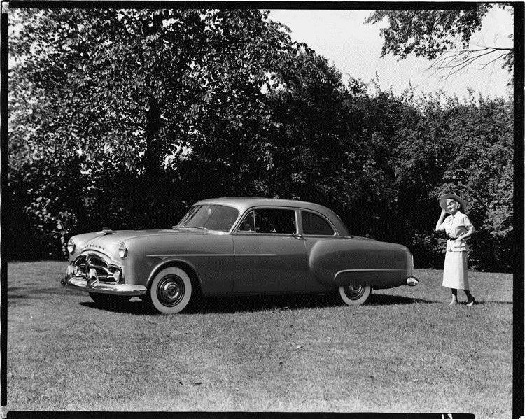 1951 Packard 200 sedan, parked on grass, female standing near rear