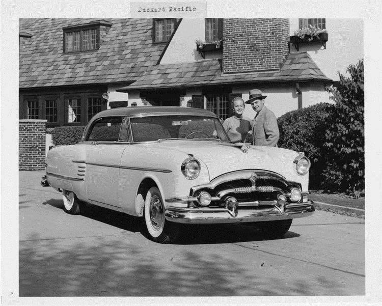 1954 Packard Pacific, couple standing at driver's door, parked in driveway of house