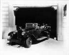 1928 Packard touring car leaving garage with female driver and passengers