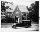 1930 Packard sedan limousine, left side view, parked on street in front of large brick home