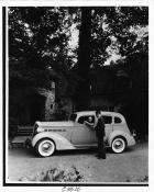 1937 Packard sedan, female driver, parked in front of home, male standing at driver's door