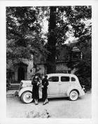 1937 Packard sedan, left side view, parked in front of home, two females standing at driver's door
