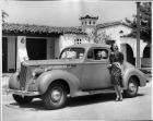 1940 Packard business coupe, parked on street in front of house, female behind wheel