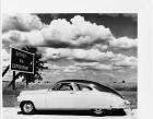 1948 Packard club sedan on road with female driver, by sign 'Detroit Via Expressway'