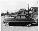 1949 Packard sedan, left side view, parked in lot, houses in background