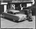 1951 Packard sedan parked in driveway in front of house and female with luggage