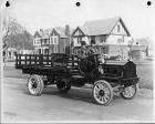Early 1900s Packard truck, right side view, parked on residential street houses in background, two m