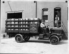 Early 1900s Packard truck full of wooden crates, parked on street next to brick building